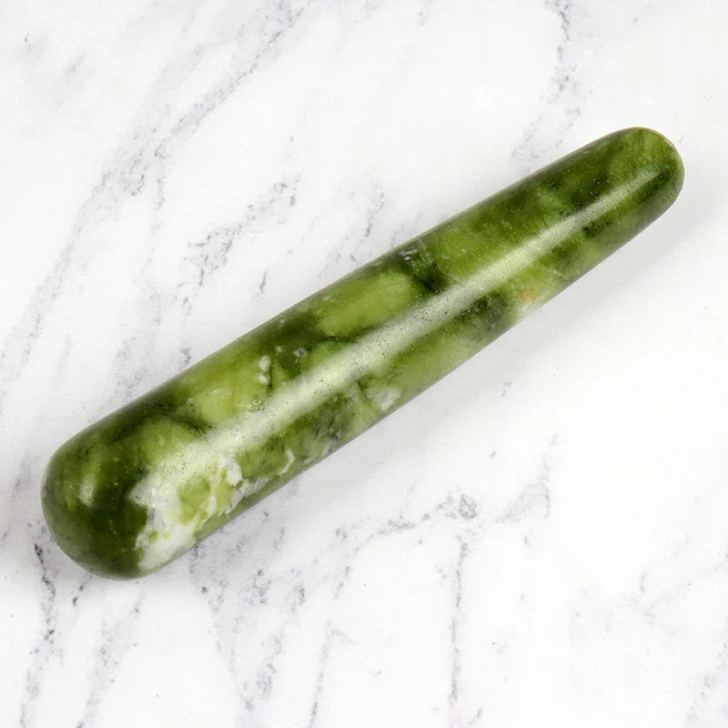 Natural green stone crystal face massager on marble background, ideal for skincare and relaxation.