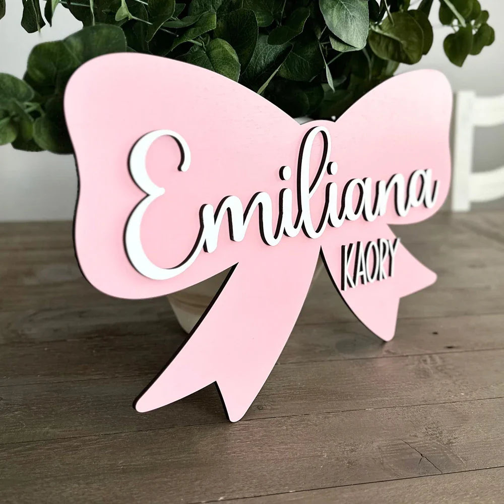 Customized pink wood baby name sign with bow for nursery room decor.