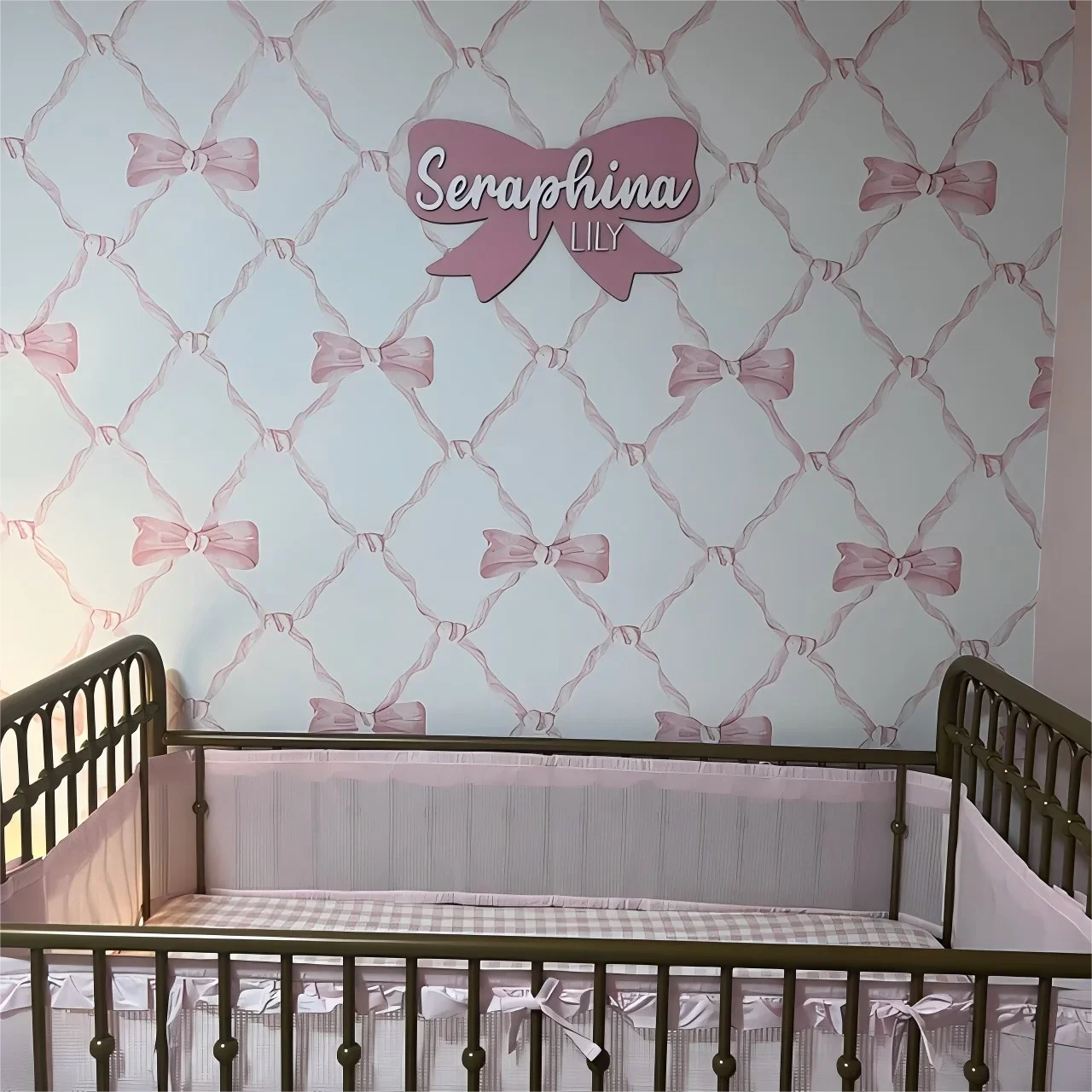 Customized wood baby name sign with pink bow decor above crib in nursery.