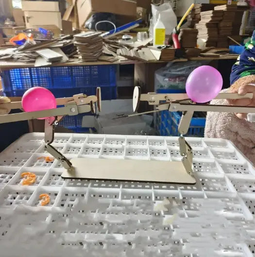 Interactive wooden figurines with movable parts holding pink balloons on a table in a workshop setting
