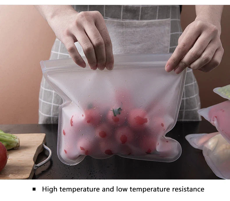 Hands holding a reusable silicone food storage bag filled with fresh tomatoes on a kitchen countertop