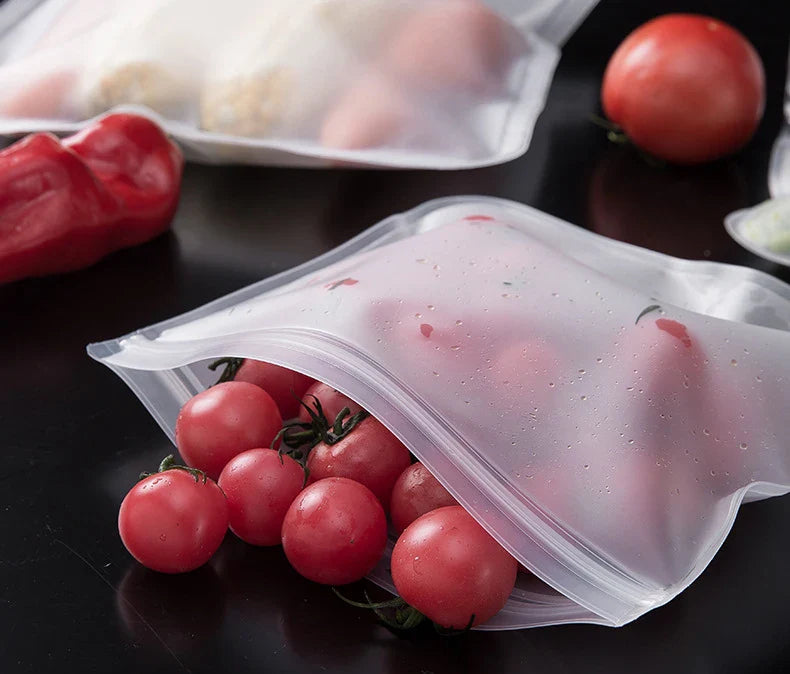Reusable silicone food storage bags with zip seal holding cherry tomatoes on black surface