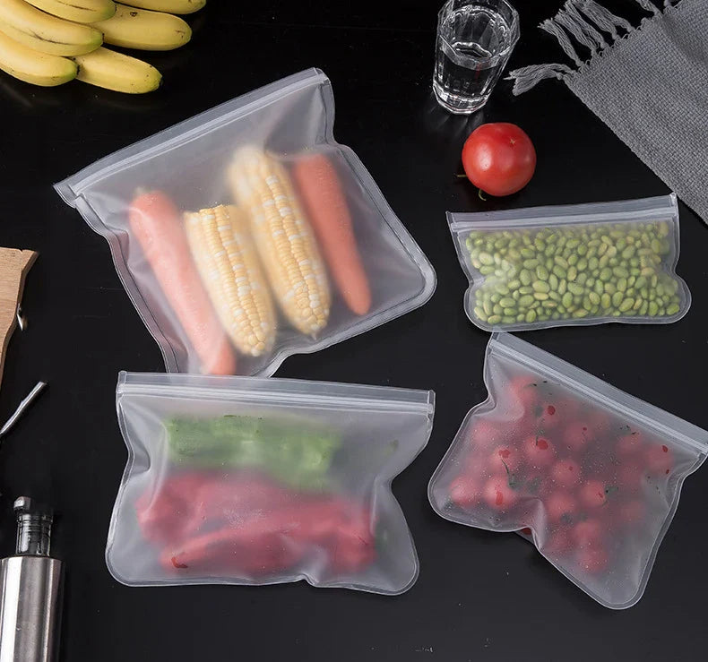 Reusable silicone food storage bags with zip closure holding vegetables and fruits on a black surface