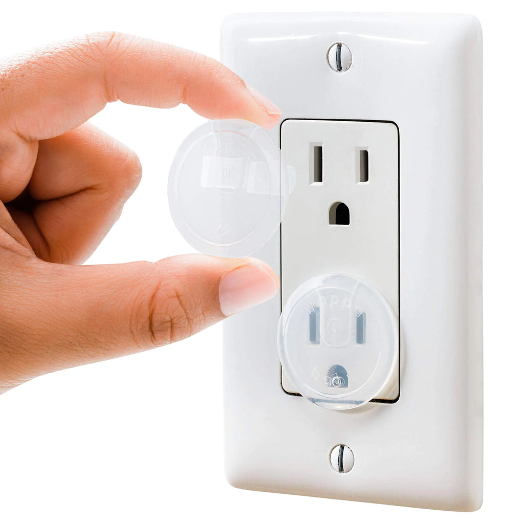 Hand installing clear baby safety outlet plug cover on electrical socket for childproofing home.