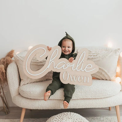 Customized wood baby name sign with child holding it on sofa, nursery room decor.