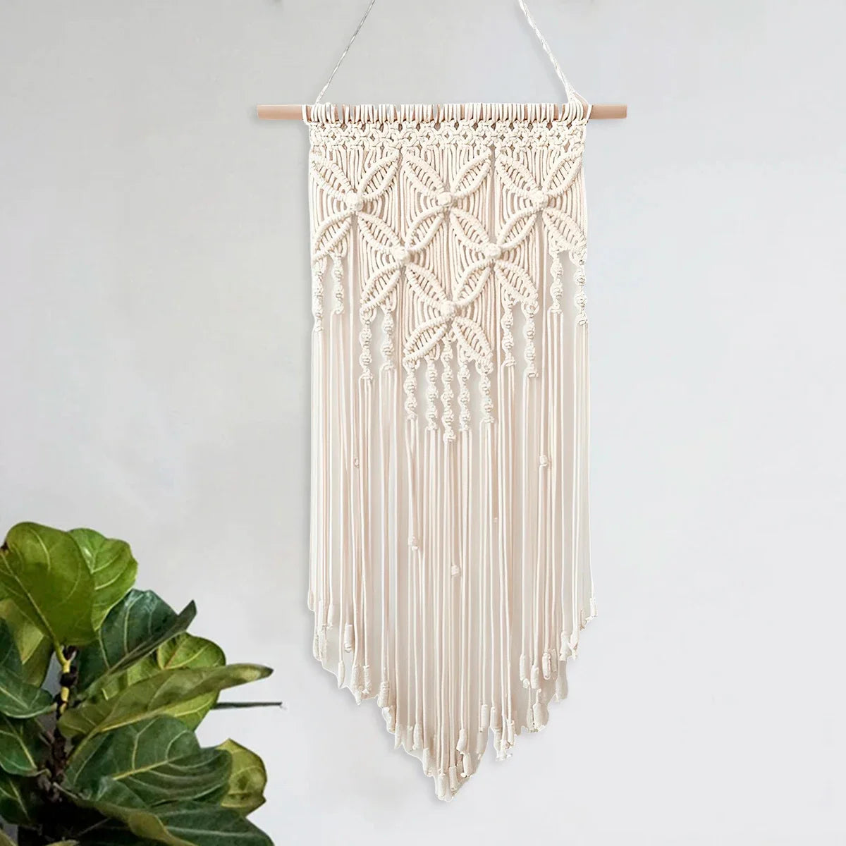 Handmade macrame wall hanging tapestry with intricate designs and tassels, made from beige cotton threads and a wooden stick, perfect for rustic home decor in living rooms or bedrooms.