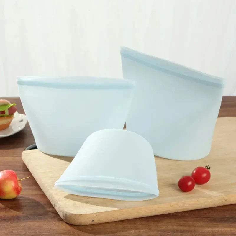 Reusable silicone food storage bags set on a wooden surface with fruit.