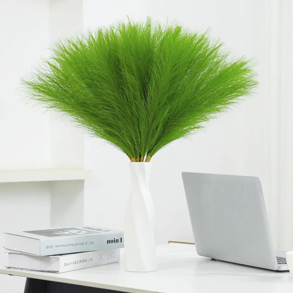 Green faux pampas grass in a white vase on a desk, enhancing home decor.