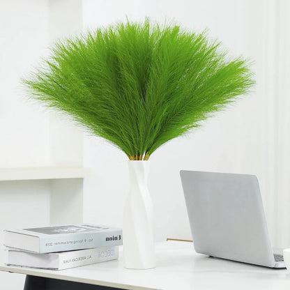 Green faux pampas grass in a white vase on a desk, enhancing home decor.