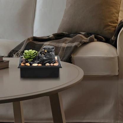 Mini tabletop fountain with light on a modern coffee table, featuring plant decor and natural pebbles for relaxation and meditation.