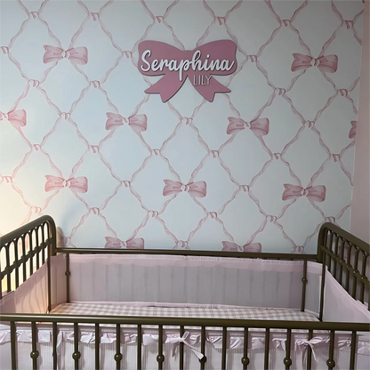 Customized wood baby name sign with pink bow decor above crib in nursery.