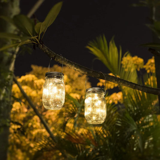 Solar mason jar lights hanging in a garden, illuminating with warm white LED glow.
