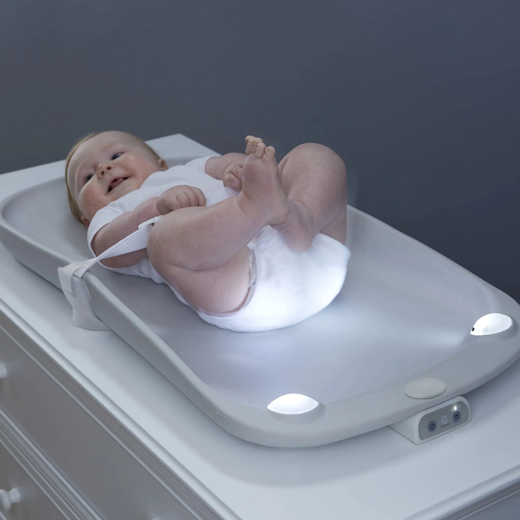 Baby lying on Contours Glow Motion Sensing Light-Up Changing Pad with soft glow lights on a dresser